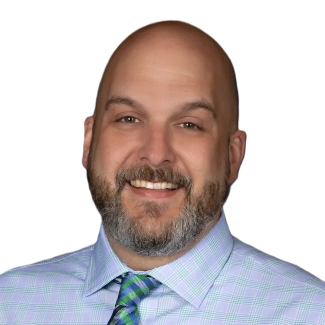 Smiling bald man with a beard, wearing a light blue plaid shirt and green tie, against a dark gradient background.